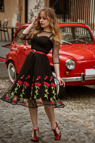 Influencer wears our mesh sleeved swing dress, in black, with embroidered red roses, in front of an old red car