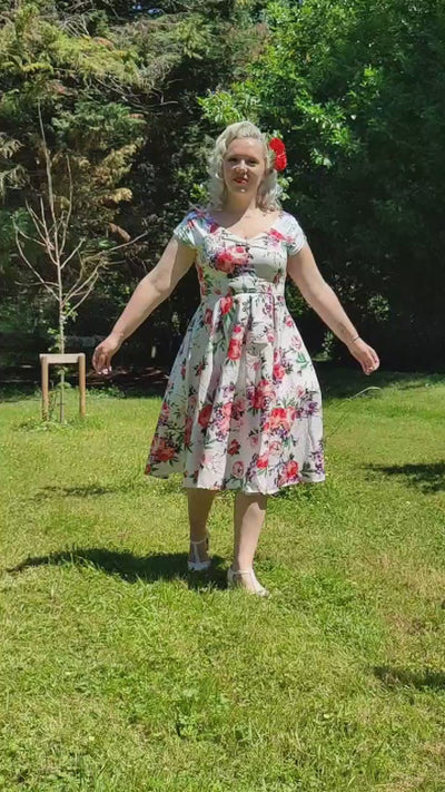 Video of a woman wearing our Lily, off-shoulder 50's Evening Dress in White, with pink and purple flowers, twirling