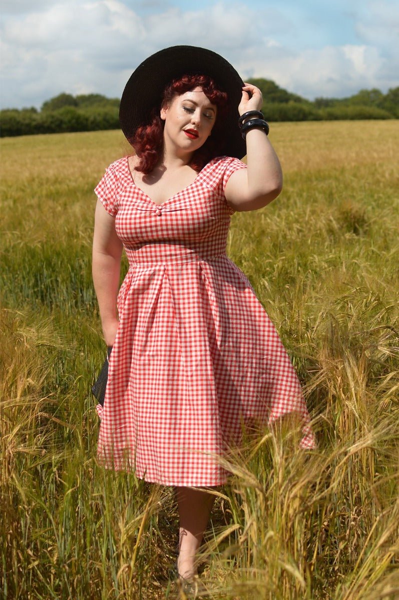 Woman wears our short sleeved, off-shoulder flared dress, in red gingham print, in a wheat field
