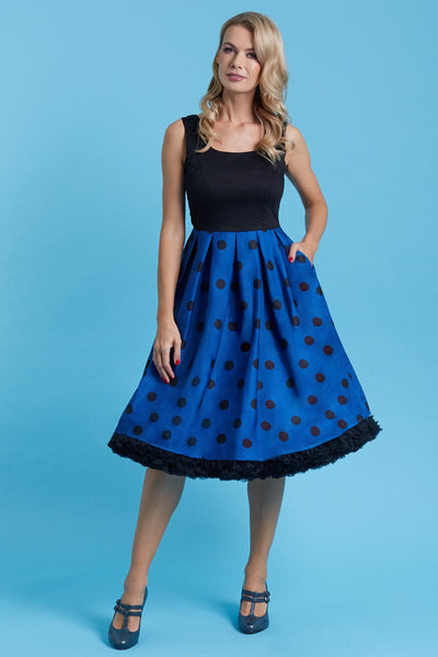 Model wears our sleeveless swing dress, in black, dark blue polka dot print, front view, hand in pocket