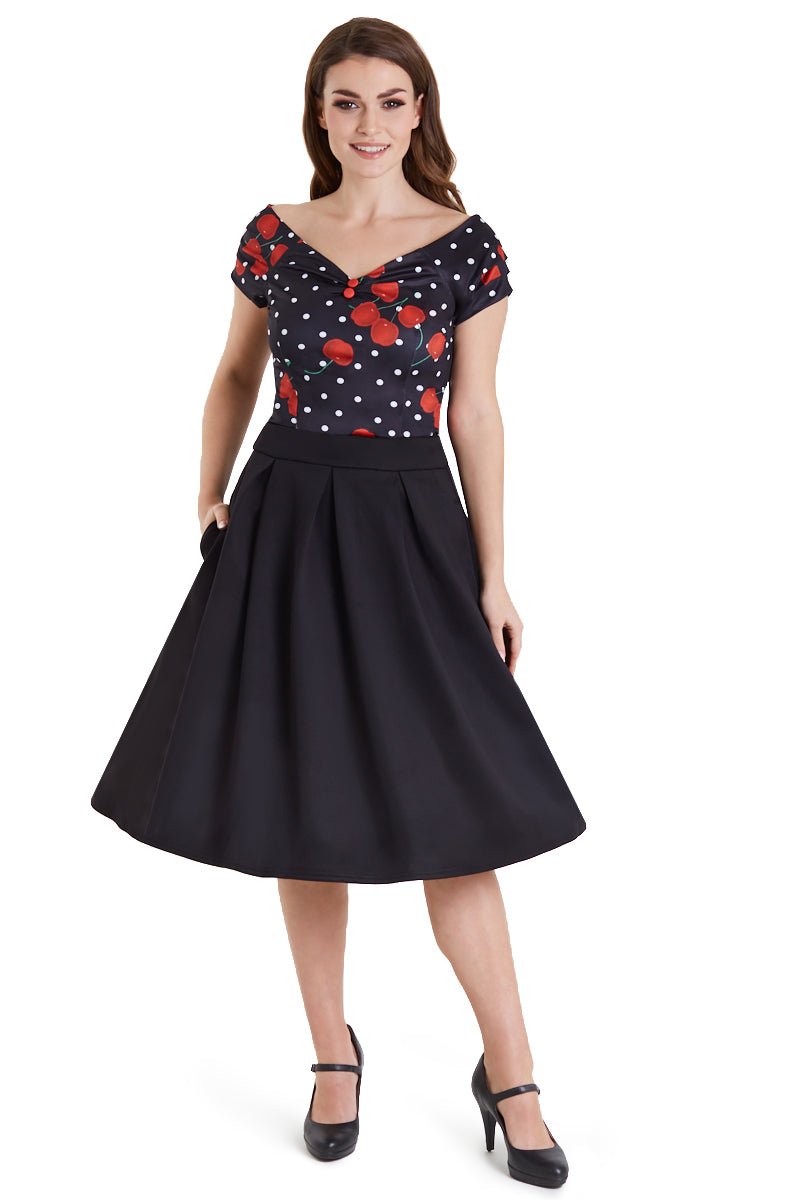 Model wears our V neck, short sleeve, off-shoulder top, in black, with red cherries and white dots, with black skirt, front view