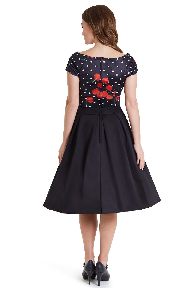 Model wears our V neck, short sleeve, off-shoulder top, in black, with red cherries and white dots, with black skirt, back view