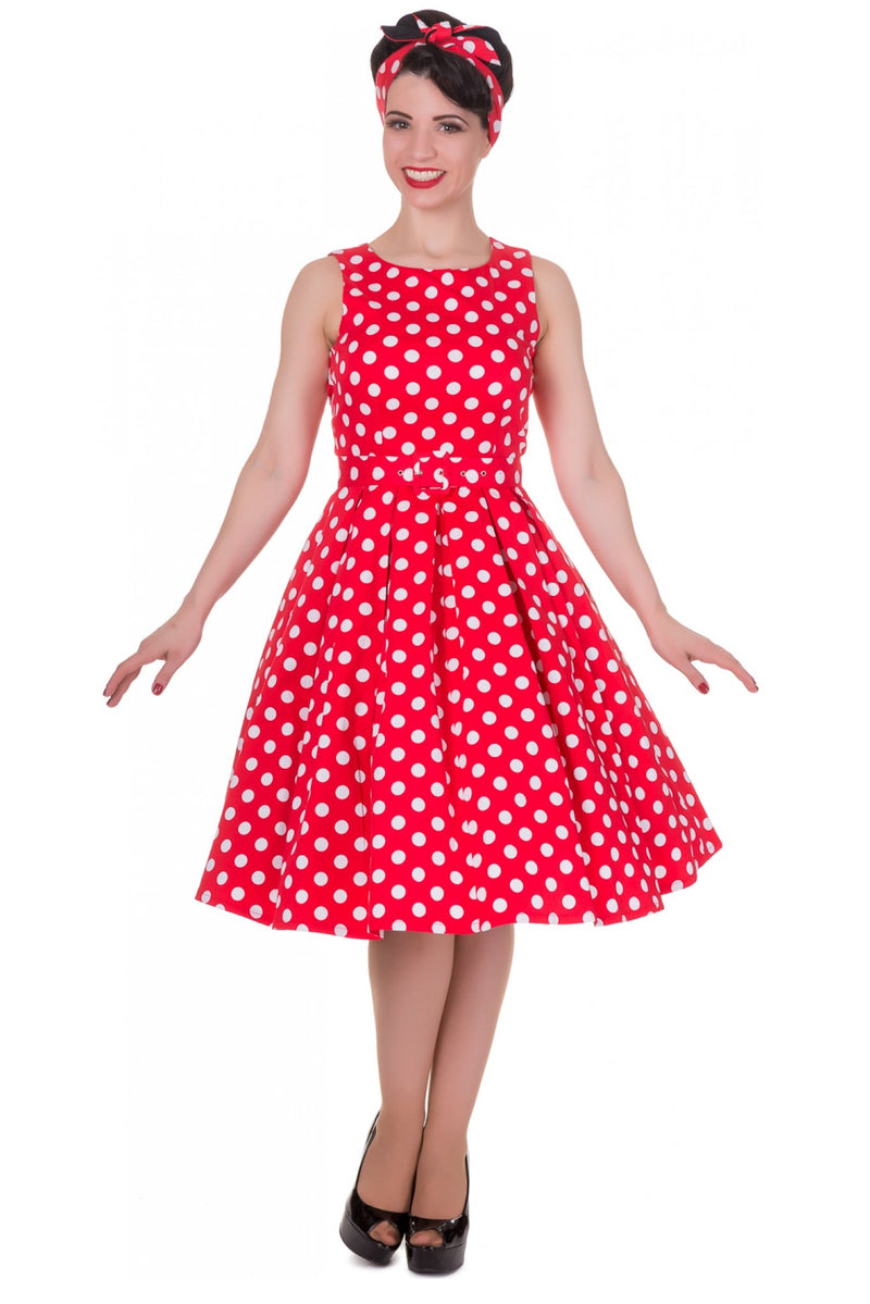 Model wearing our sleeveless Annie dress, in red, with white spots, with a matching headband,  front view
