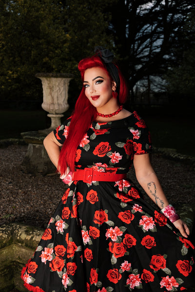 Woman wears our short sleeved swing dress, in black/red roses print, with red accessories, in front of a statue