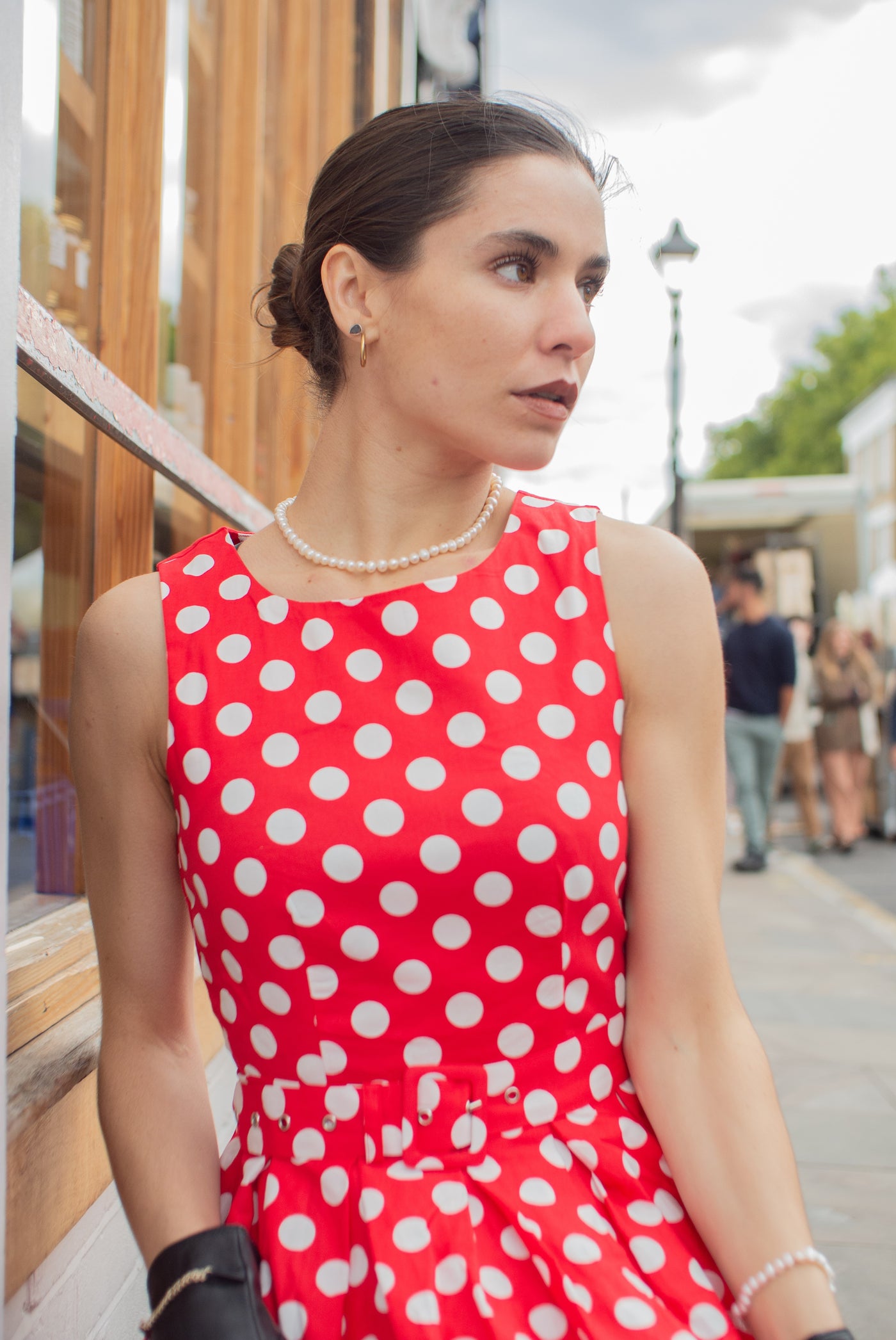 Woman wearing our sleeveless Annie dress, in red, with white spots, with accessories, outside