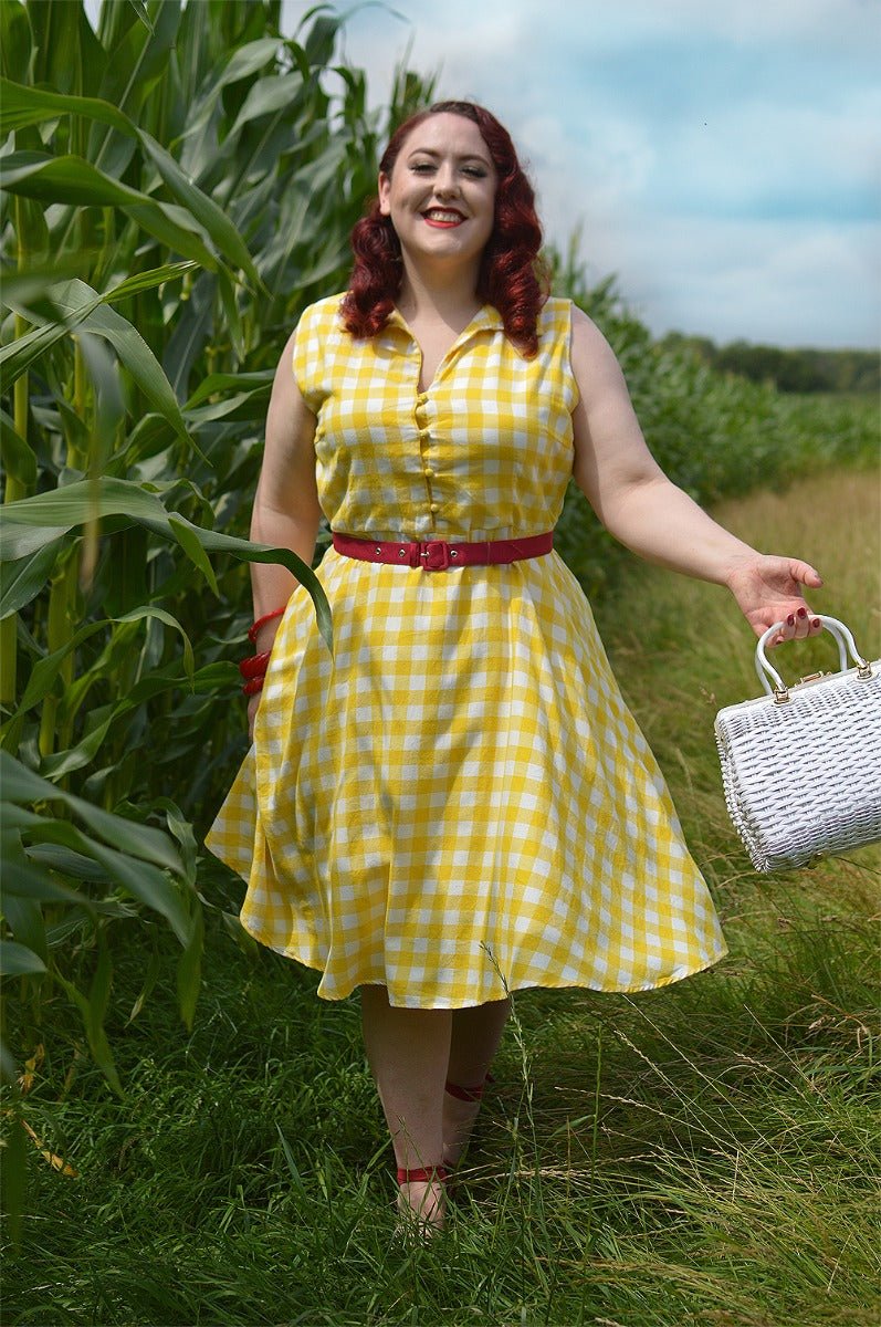 Woman wears our sleeveless button-top swing dress, in yellow/white gingham check print, in nature