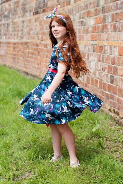 Girl wears our short sleeved swing dress, in navy blue unicorn, space rainbow print, side view