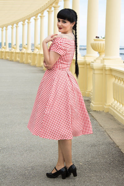 Woman wears our short sleeved, off-shoulder flared dress, in red gingham print, side view
