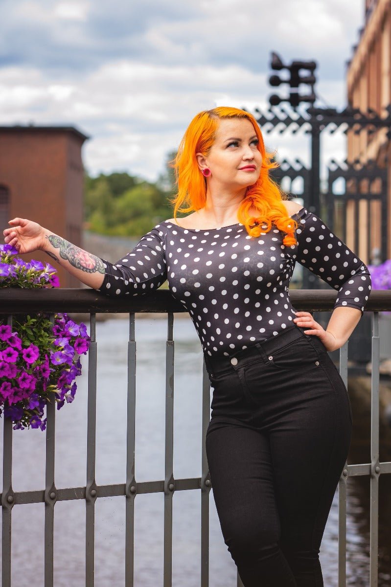 Woman wearing our Gloria off-shoulder Top in Black/White polka dot print, with black jeans, front view