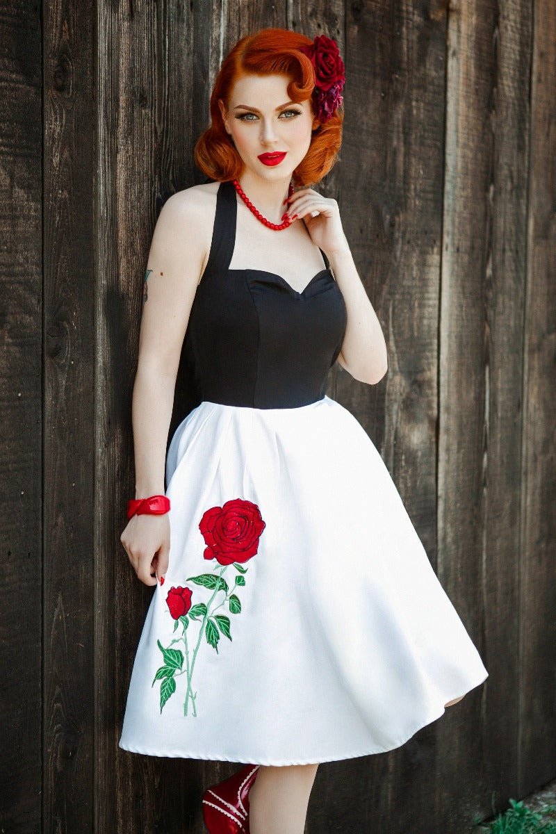 Model wearing halterneck dress in black and white with embroidered red rose on the skirt
