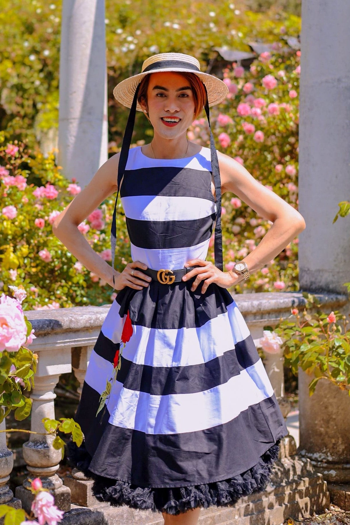 Customer wears the black and white striped Annie swing dress, with embroidered red rose on the skirt, with petticoat, in a garden