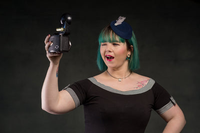 Customer wears our short sleeved round neck top, in black, with stripe trims, takes a selfie on a vintage camera