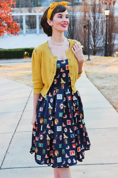 Customer wears our sleeveless Amanda swing dress, in navy blue, with framed dog art print, with mustard cardigan and headband