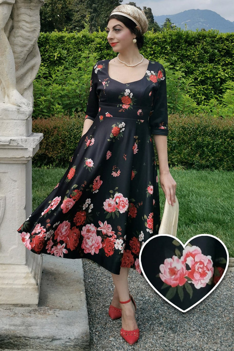 Woman wears our long sleeved, midi dress in black/pink floral print, in a public space