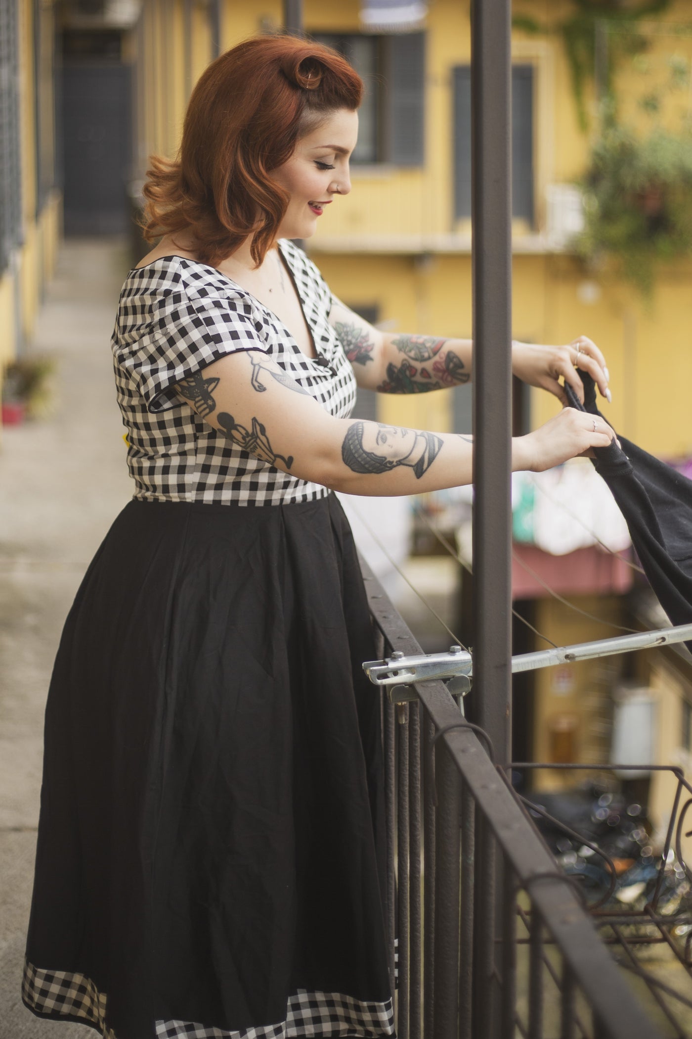 Woman wears our Lily Off Shoulder Black/White Gingham Swing Dress, on a balcony 