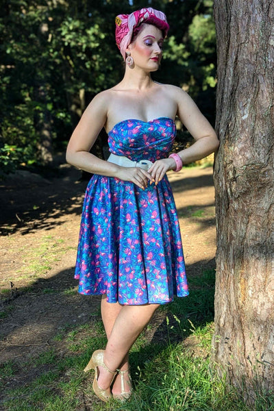 Front view of a model wearing our strapless swing dress in purple/pink flamingo print, standing next to a tree