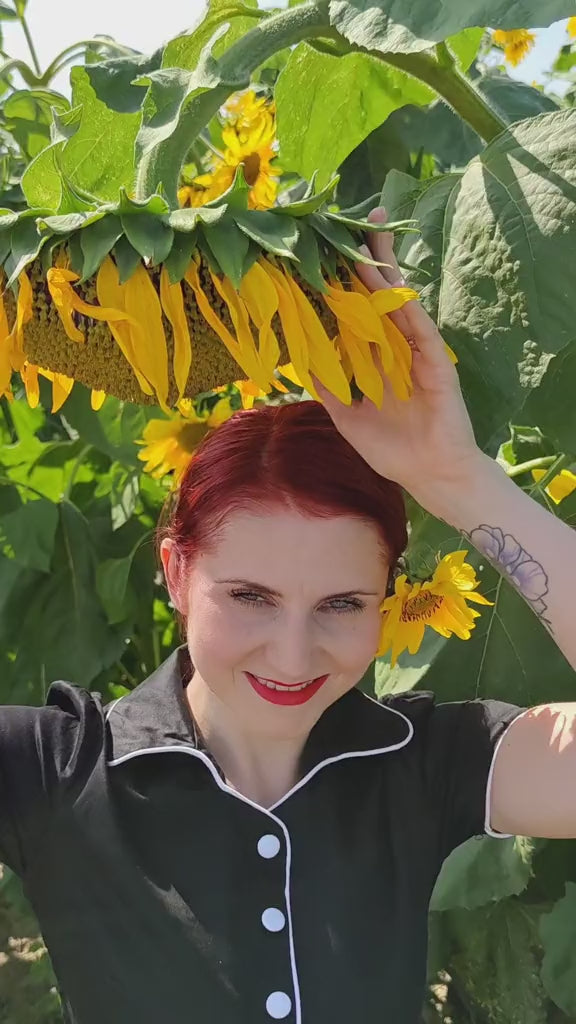 Video of a woman wearing our Short sleeve Penelope diner button top dress, in black and white, in a field of sunflowers