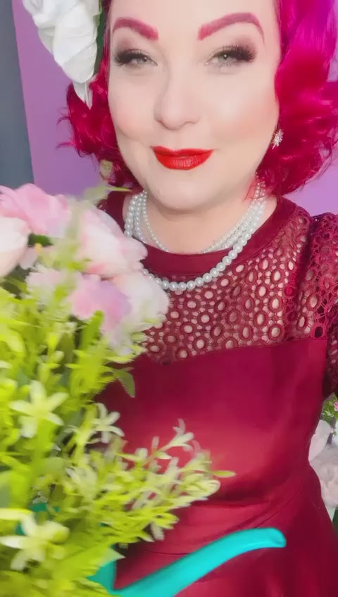 A video of Ms. Maggiebowpinup holding a flower pot, wearing our  Tess Lace Sleeved Dress in Burgundy.