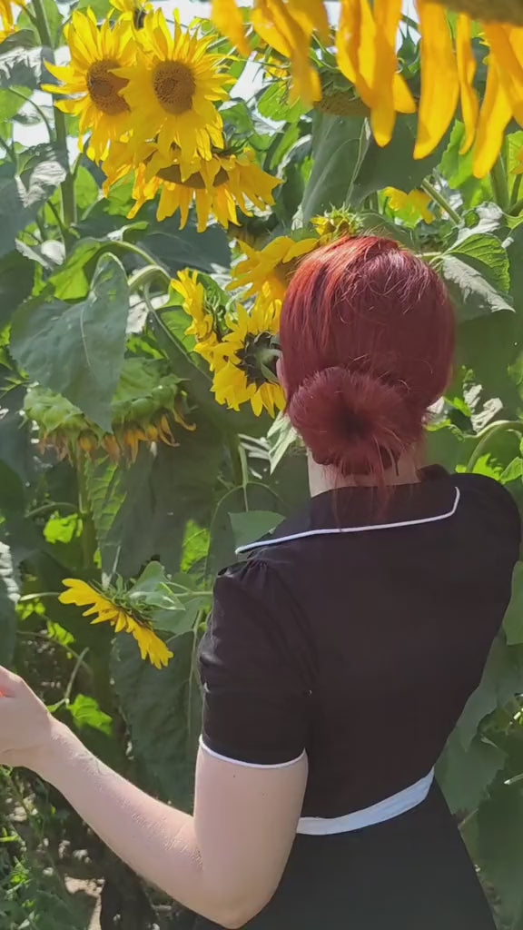 Video of a woman wearing our Short sleeve Penelope diner button top dress, in black and white, in a field of sunflowers