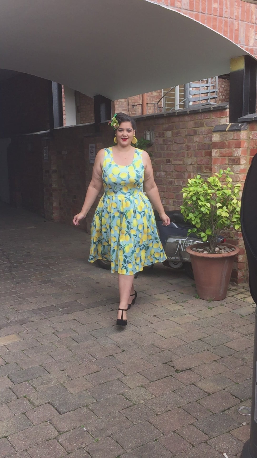 Woman walking wearing a Light Blue Sleeveless Dress with Lemon Print.