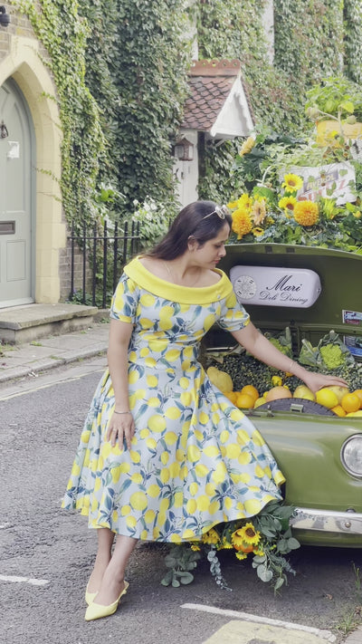 Woman wears our bateau short sleeved swing dress, in blue/yellow lemon print, by a fruit car