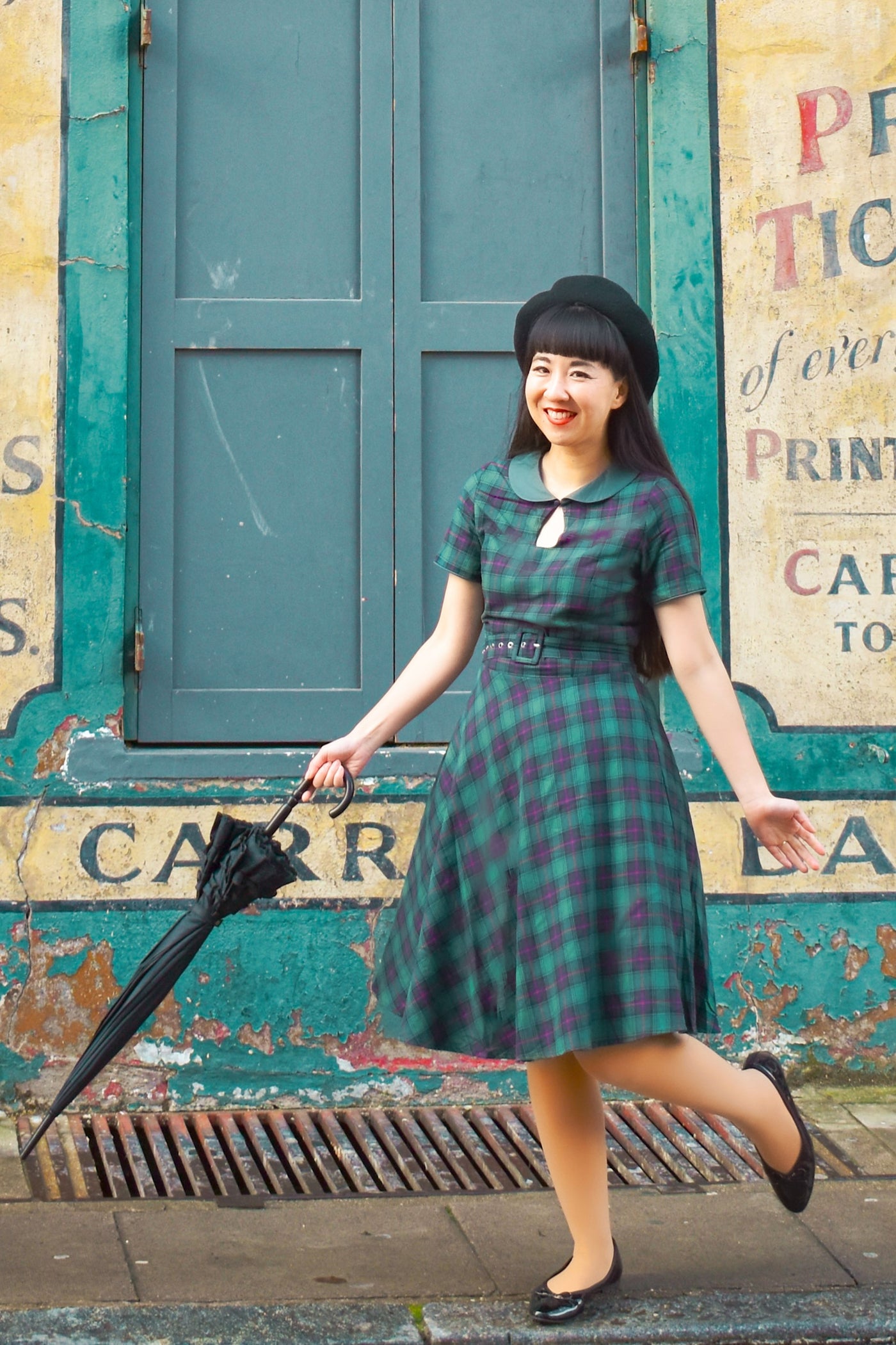 Woman wearing Evelyn Retro Check Swing Dress in Green, with umbrella, front view