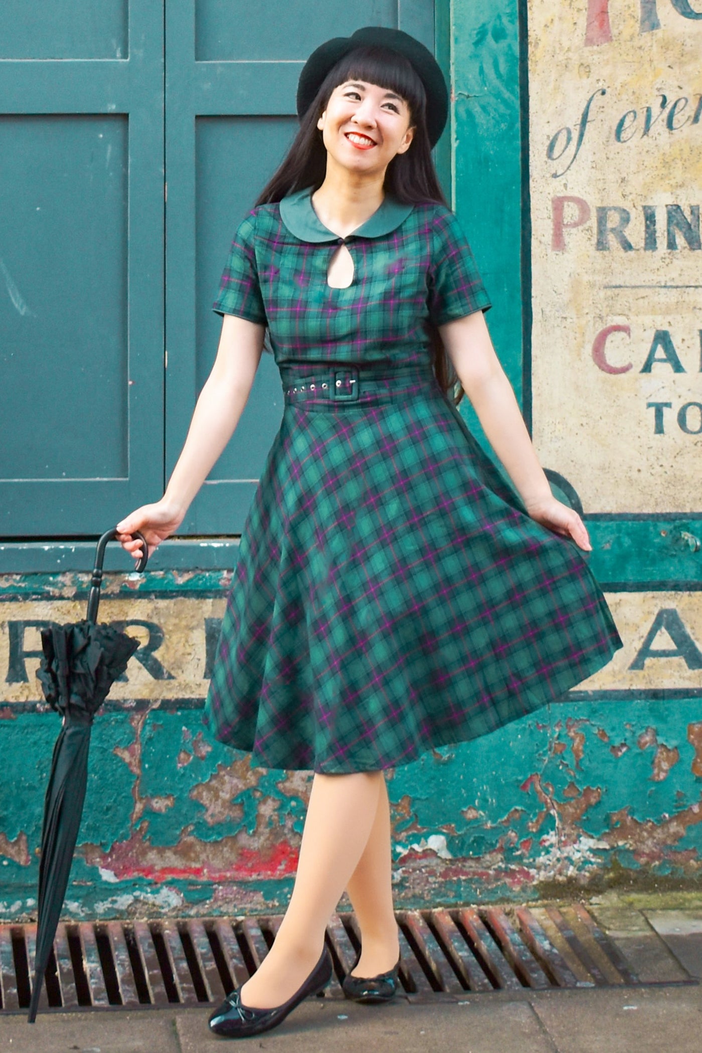 Woman wearing Evelyn Retro Check Swing Dress in Green, with umbrella, front view
