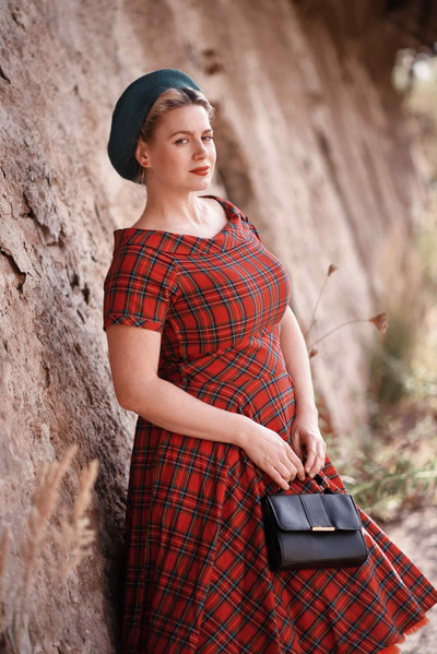 Customer wears our short sleeved flared dress, in red tartan print, with accessories, in a wood