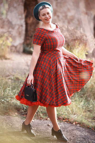 Customer wears our short sleeved flared dress, in red tartan print, with accessories, in a wood.