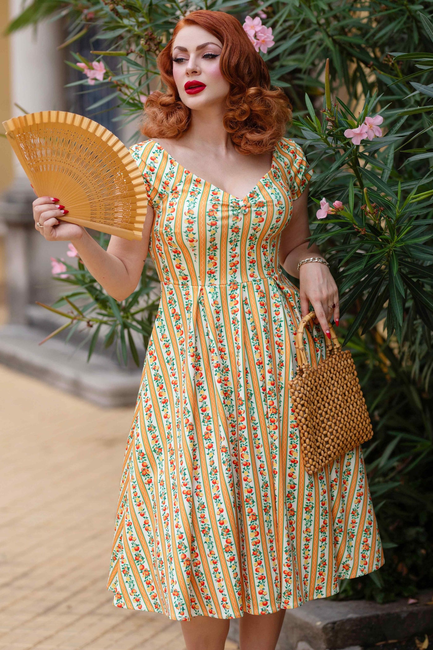 A model wearing a Sicilian Orange Stripe Swing Dress, holds skirt