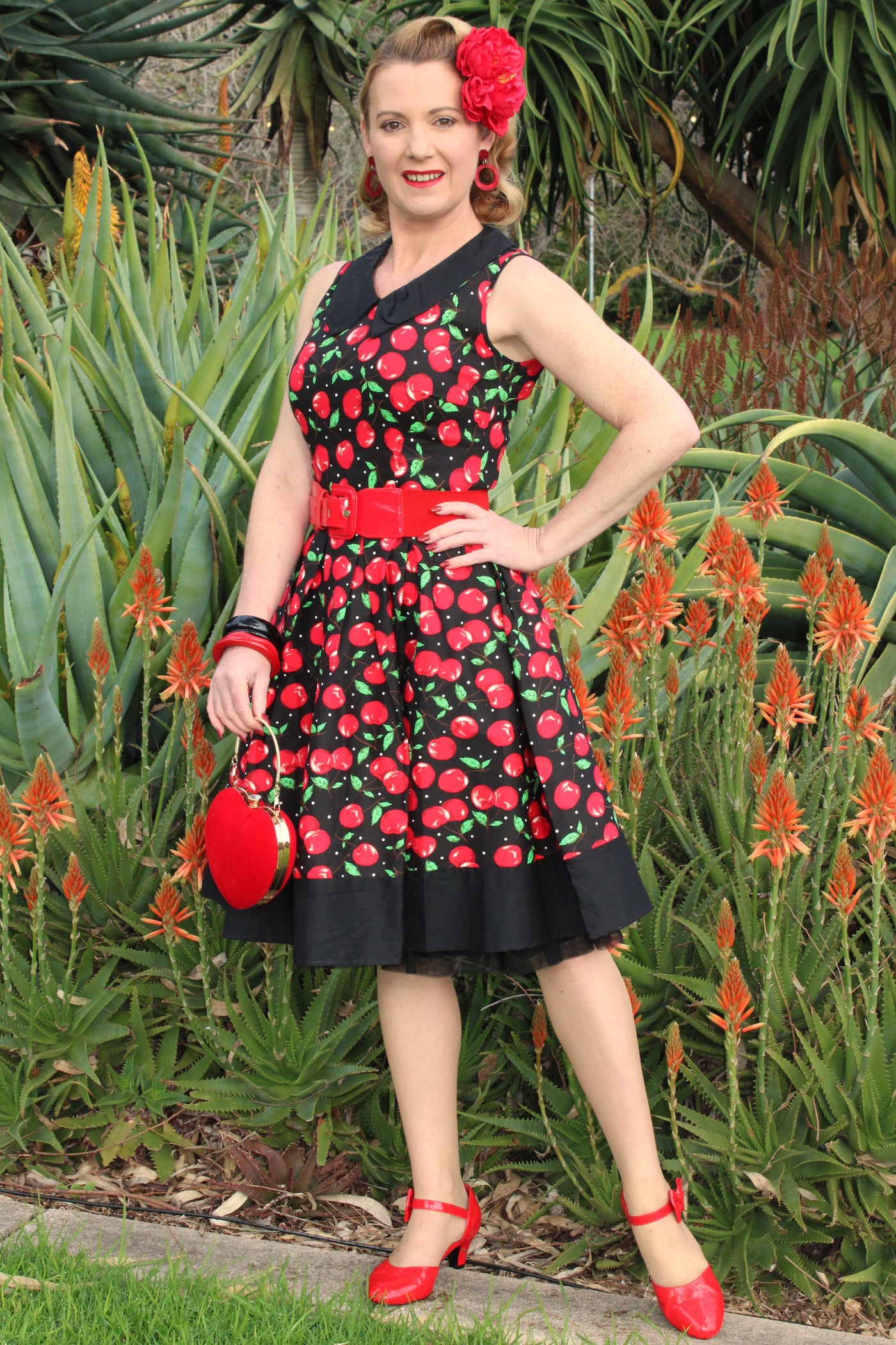 Woman wearing our sleeveless Hazel in black/red cherry print, with red belt and accessories