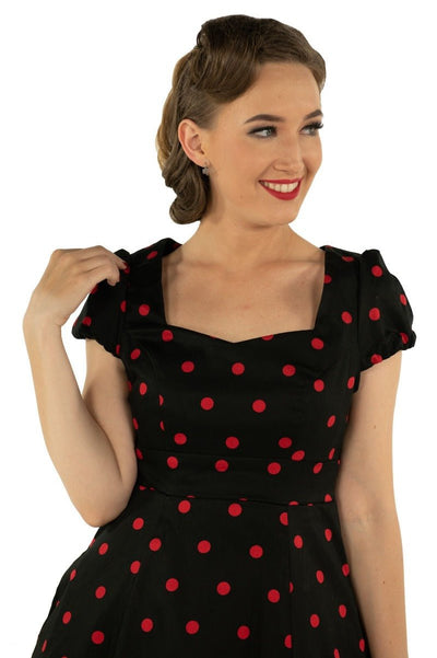 Model wears Claudia cap sleeve dress in black, with red polka dots, close up  view