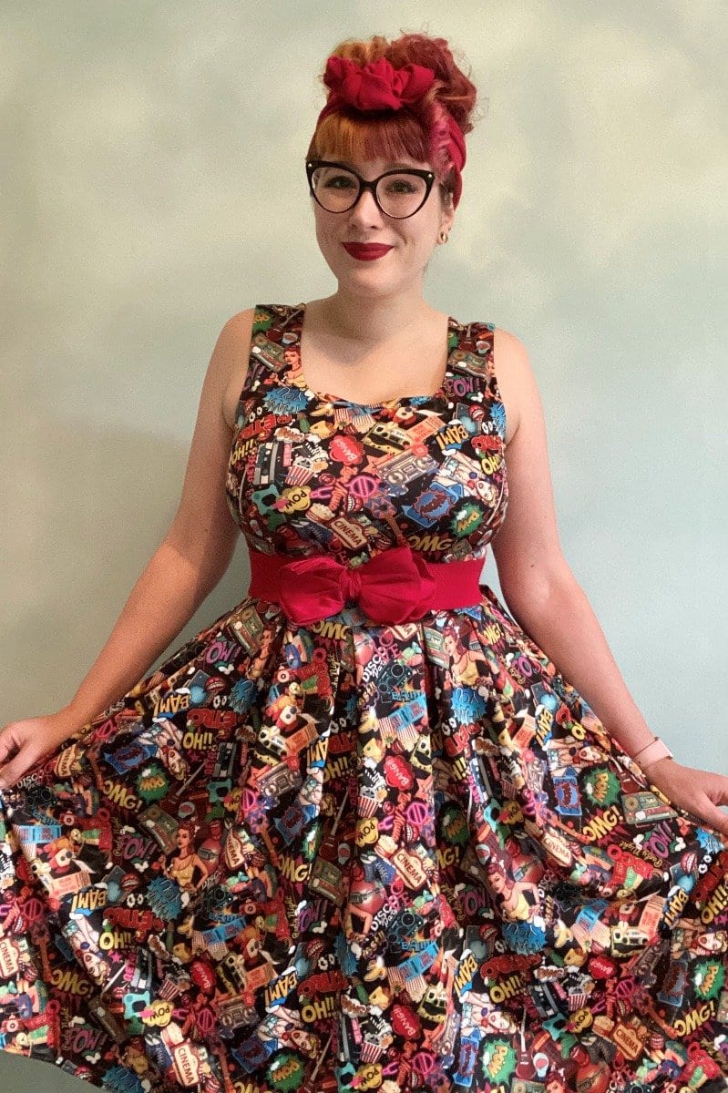 woman wears our Amanda dress, in colourful pop art comic print, whilst holding the skirt