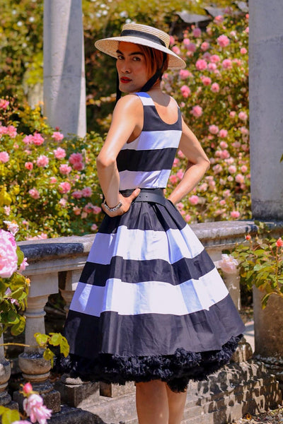 Customer wears the black and white striped Annie swing dress, with petticoat, in a garden