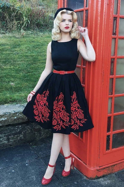 Woman wearing Annie Embroidered Roses Swing Dress in Black/Red, in front of a red telephone box