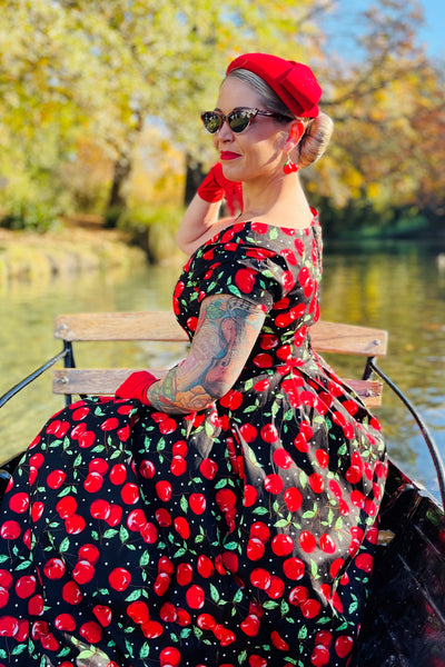 Woman wears our V neck midi flared dress, in black, red cherry print, with red accessories, on a boat