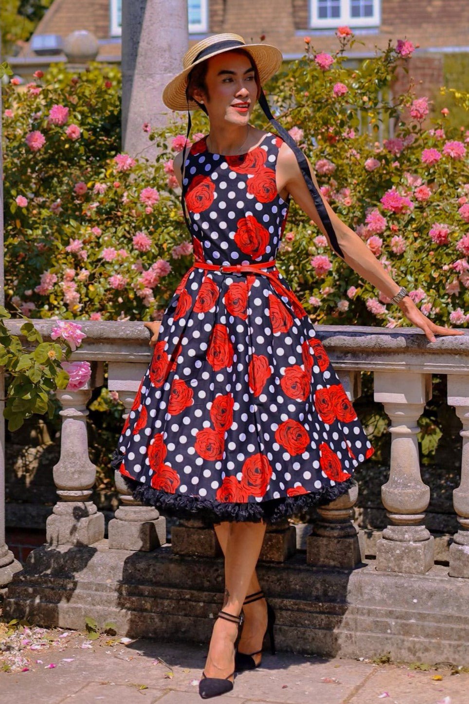 Customer wears our Annie retro dress in black/red roses and white spot print, in a garden