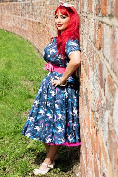 Influencer wearing blue bateau neckline dress with unicorn rainbow print against a brick wall