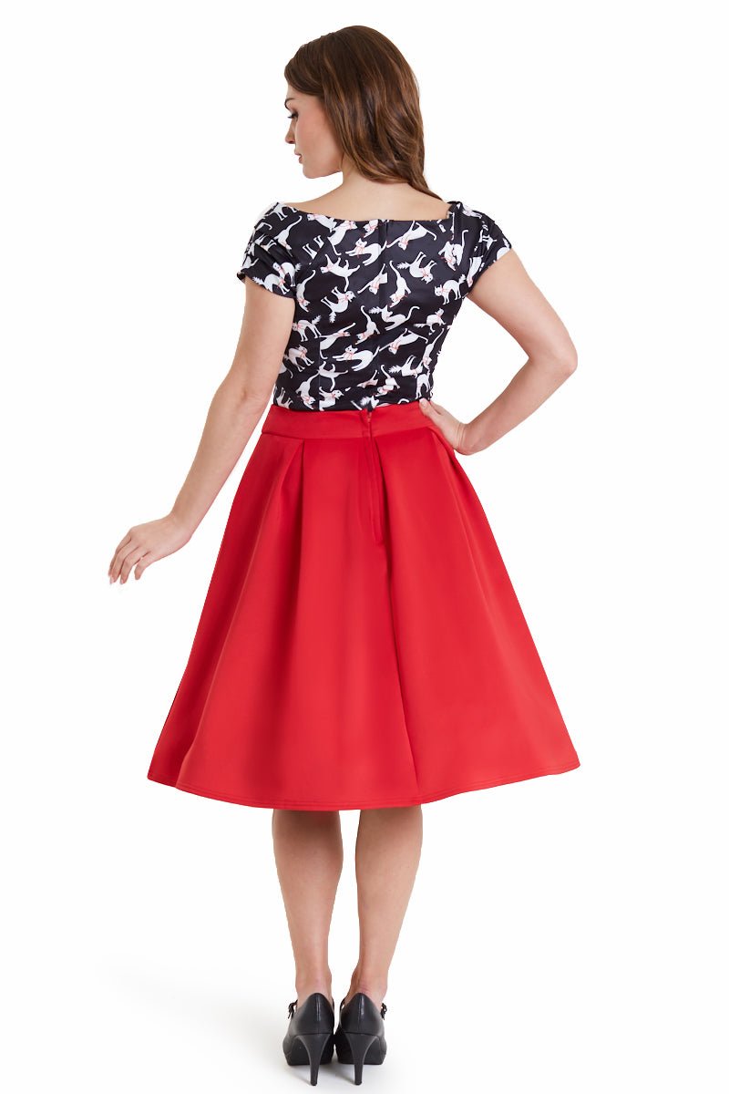 Model wears our V neck, short sleeved, off shoulder top, in black, with white cats print, with a red skirt, back view