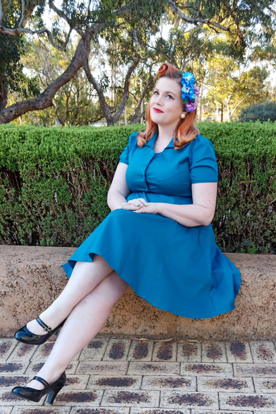 Woman wearing our short sleeved Penelope button top dress in teal blue, sitting on a wall