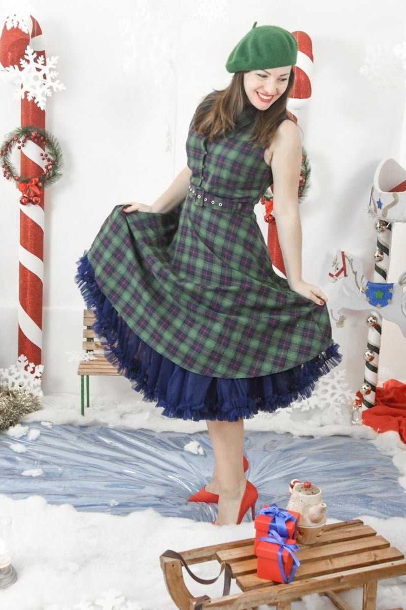 Woman wears our sleeveless Poppy button up dress in green tartan print, with a petticoat and accessories