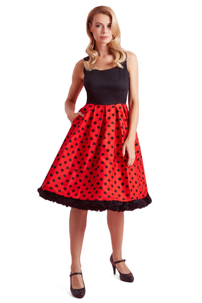 Model wears our sleeveless Amanda dress, with black top and red skirt, with black polka dot spots, front view, with hand in pocket