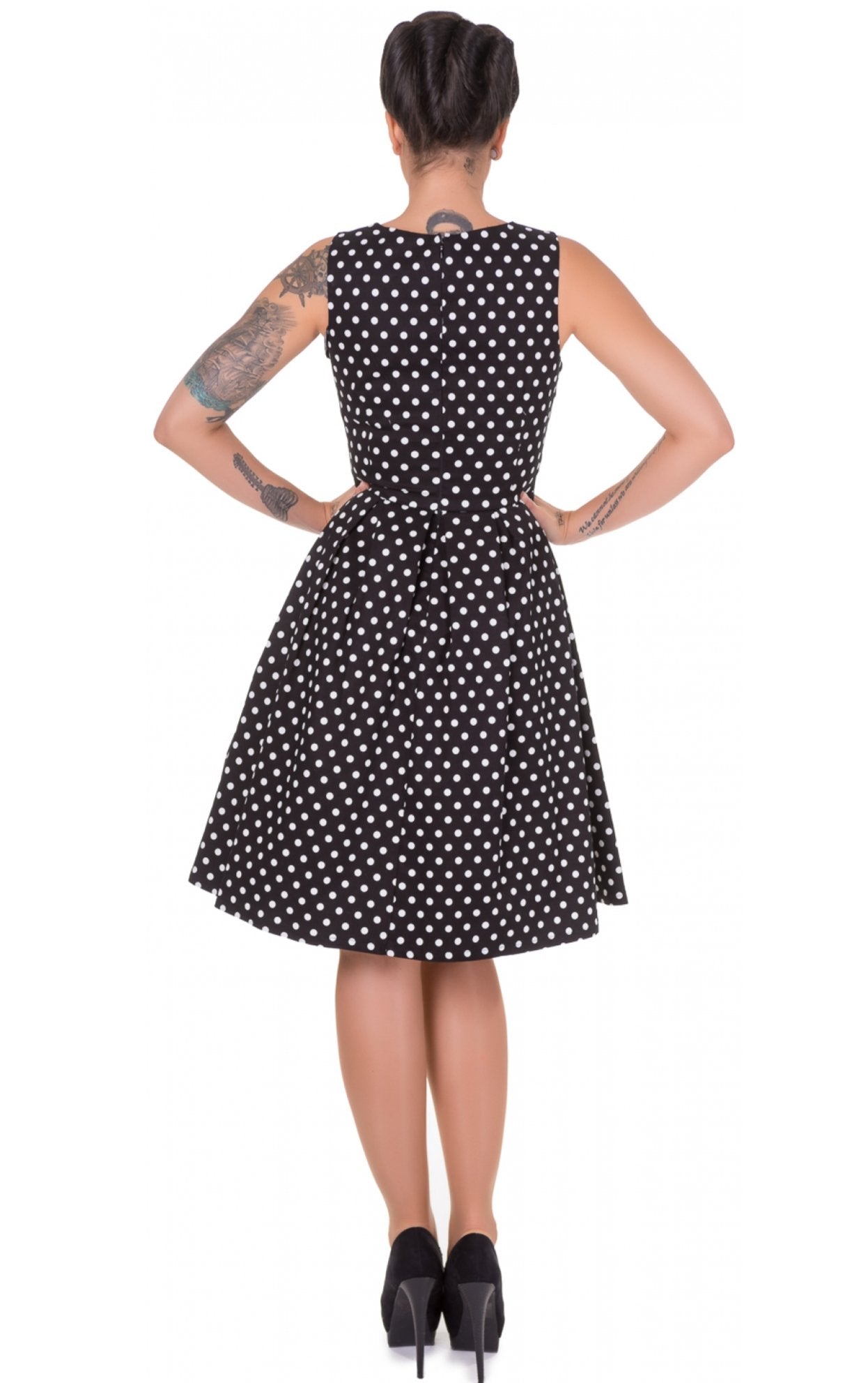 Model wears our sleeveless Lola dress in black, with white polka dots, back view