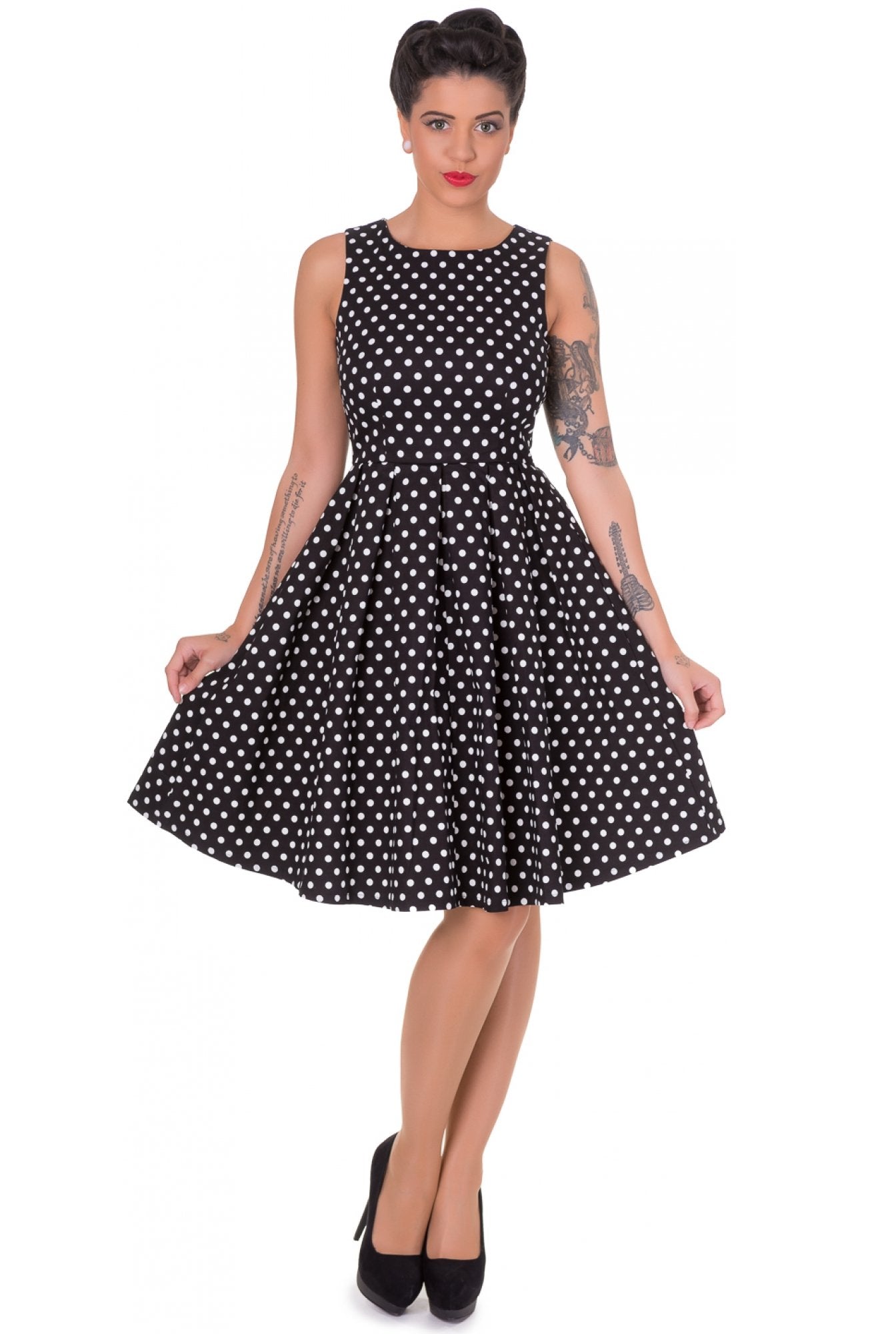 Model wears our sleeveless Lola dress in black, with white polka dots, front view