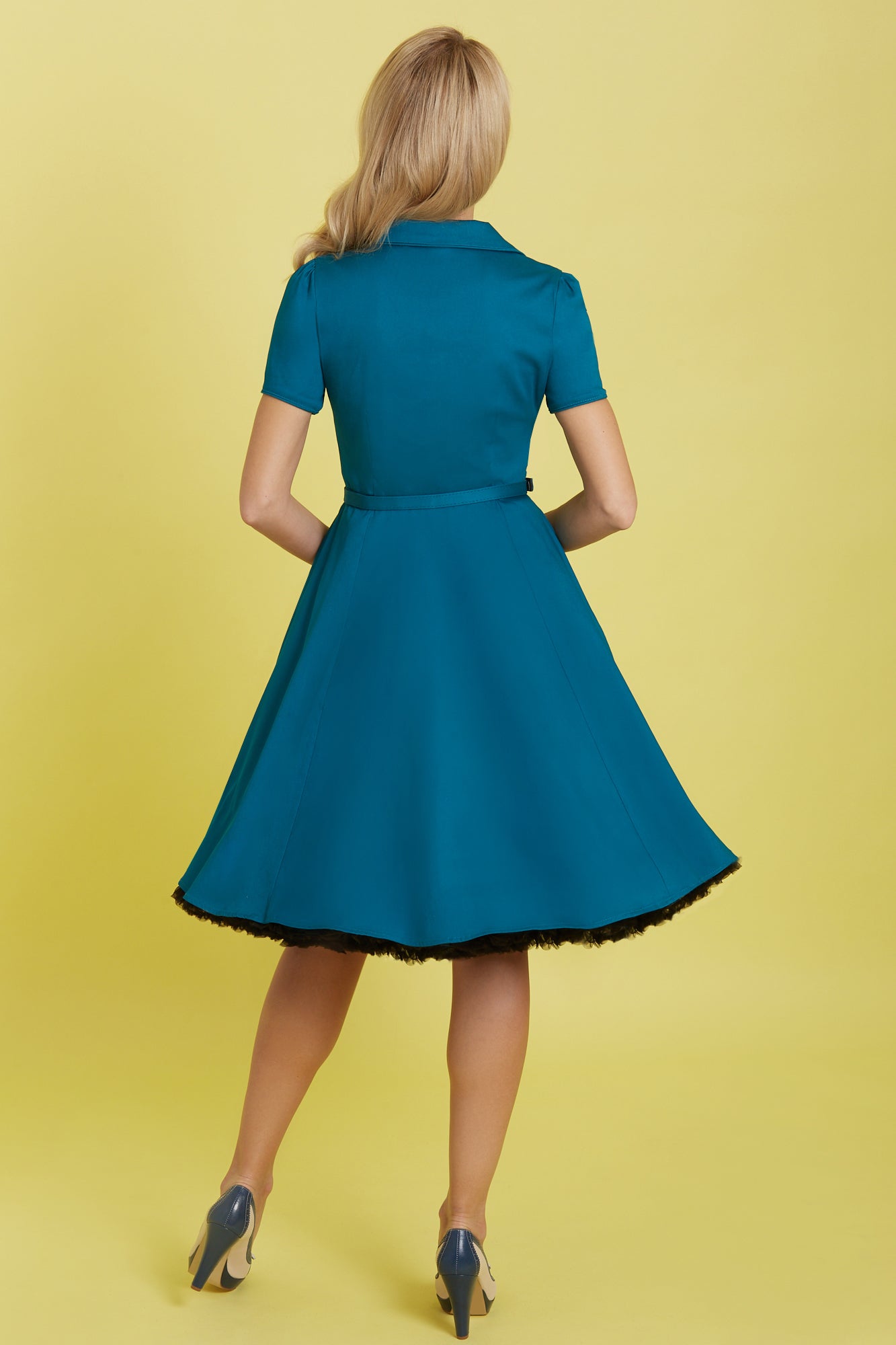 Model wearing our short sleeved Penelope button top dress in teal blue, with petticoat, back view
