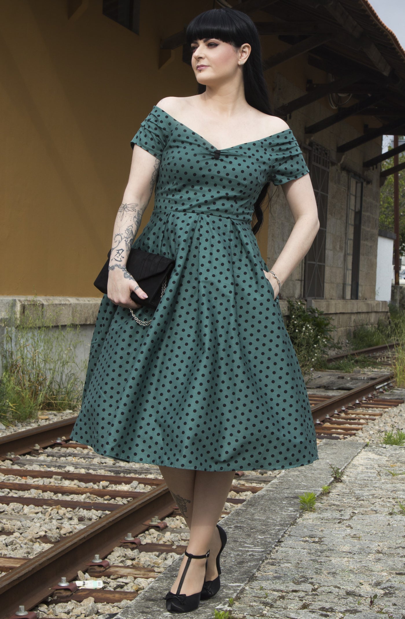 Customer wears our off shoulder flared dress, in dark green, with black polka dots, by train tracks