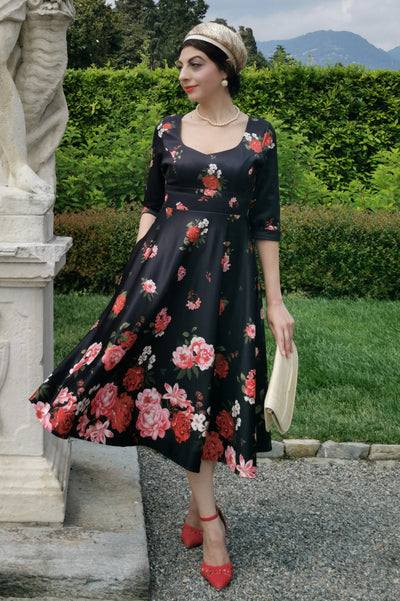 Woman wears our long sleeved, midi dress in black/pink floral print, in a public space