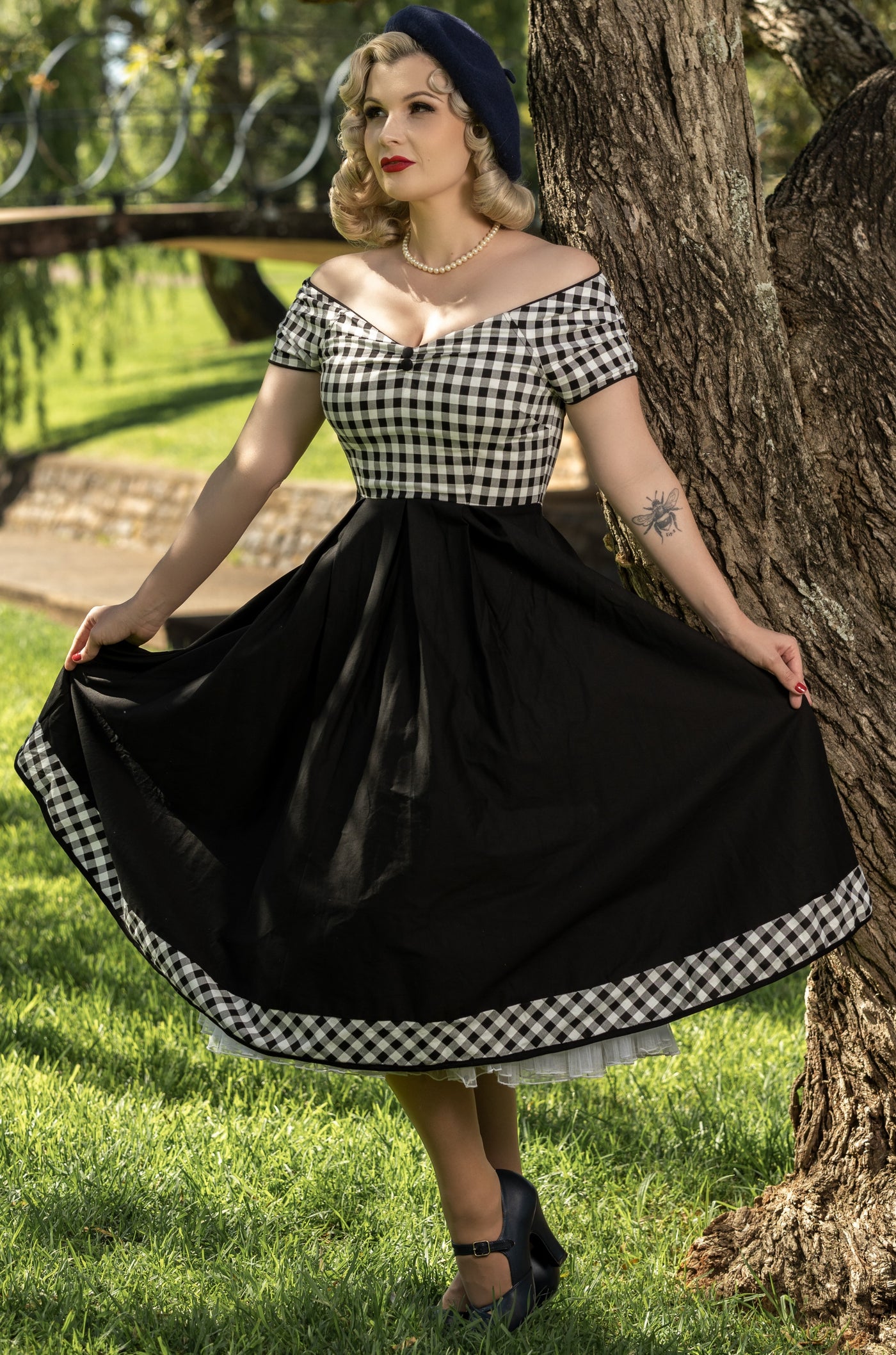 Model wearing black and white gingham swing dress, in front of a tree