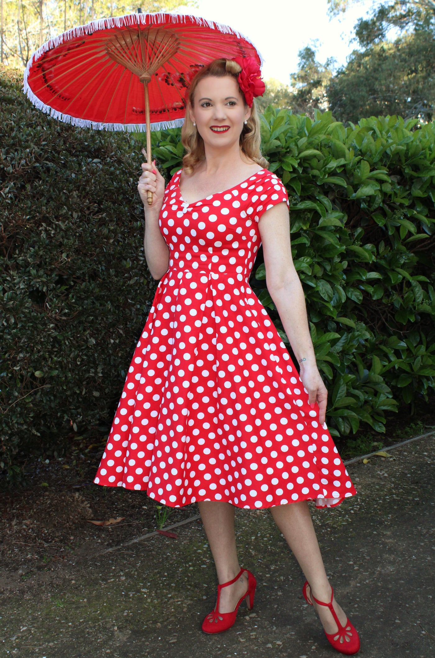 Woman wears our V neck, off-shoulder flared dress, in red, with white polka dots, front view, with red parasol