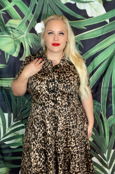 Woman wears our short sleeve Penelope dress, in brown leopard print, in front of a leaf wall